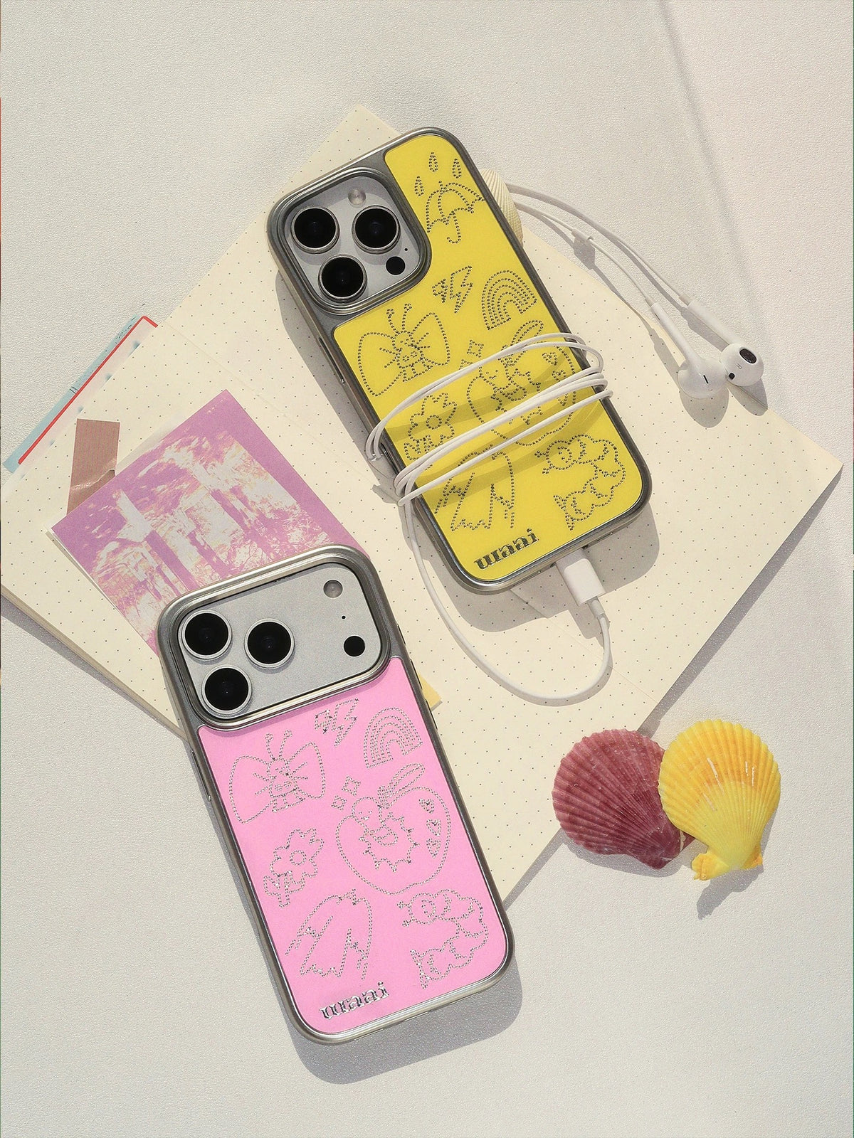 A yellow iPhone case beside the pink version, both showing silver doodles and silver colored edges.