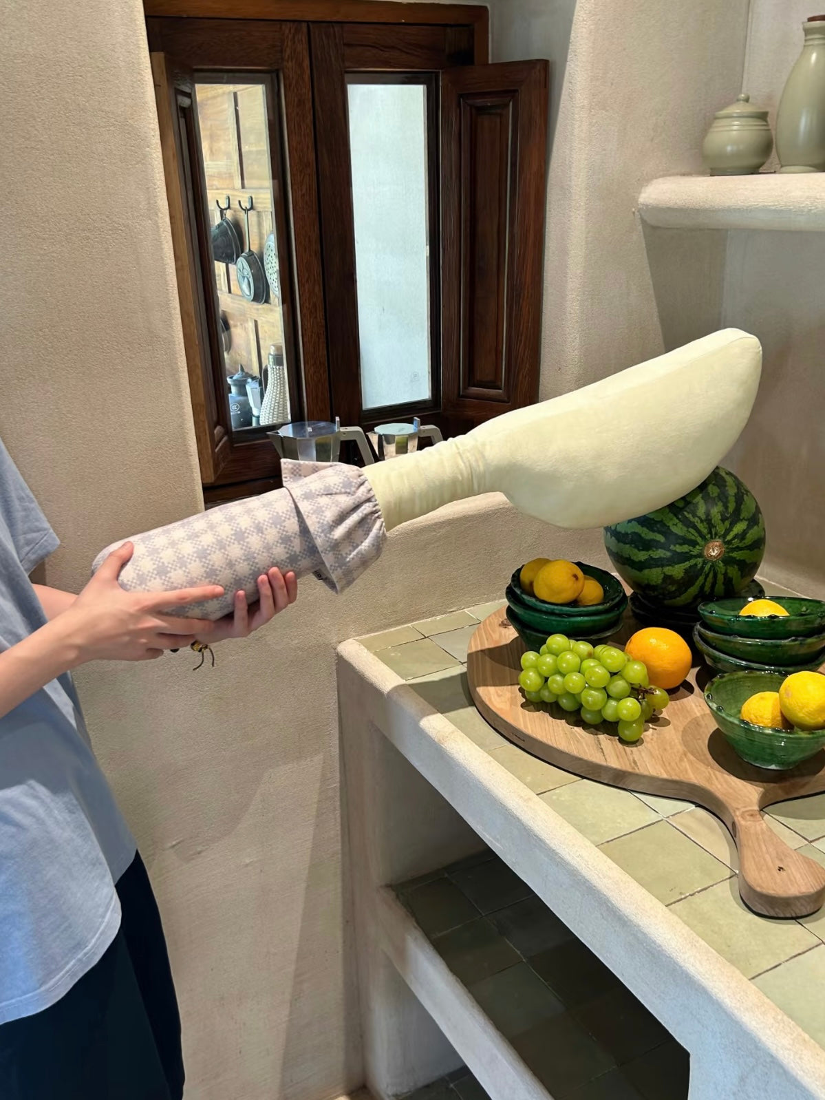 A person holds a yellow knife pillow horizontally, showing the broad curved head and checked handle.